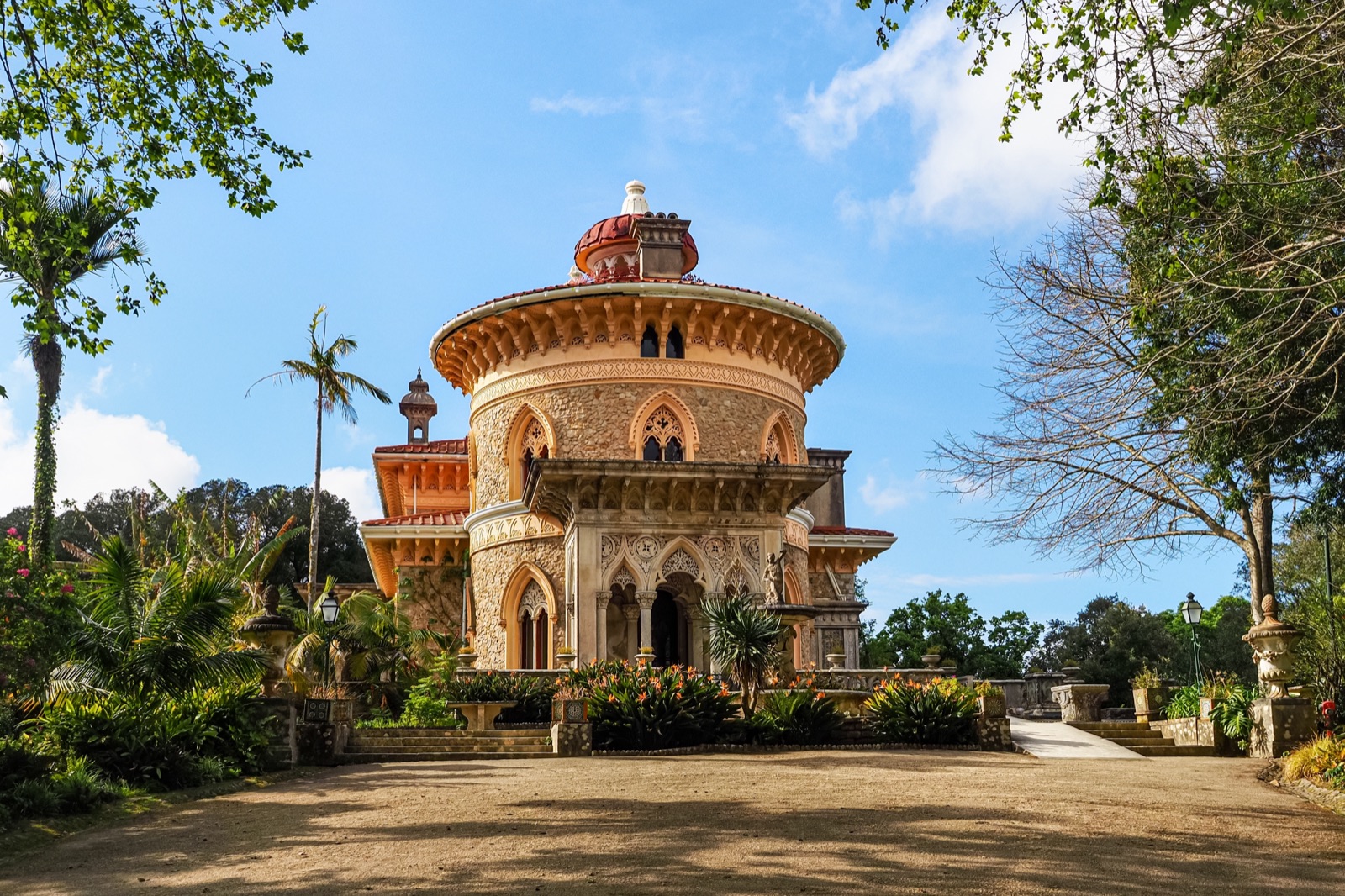 The round, ornately carved tower and arched entrance of Monserrate Palace behind palms and flowering gardens