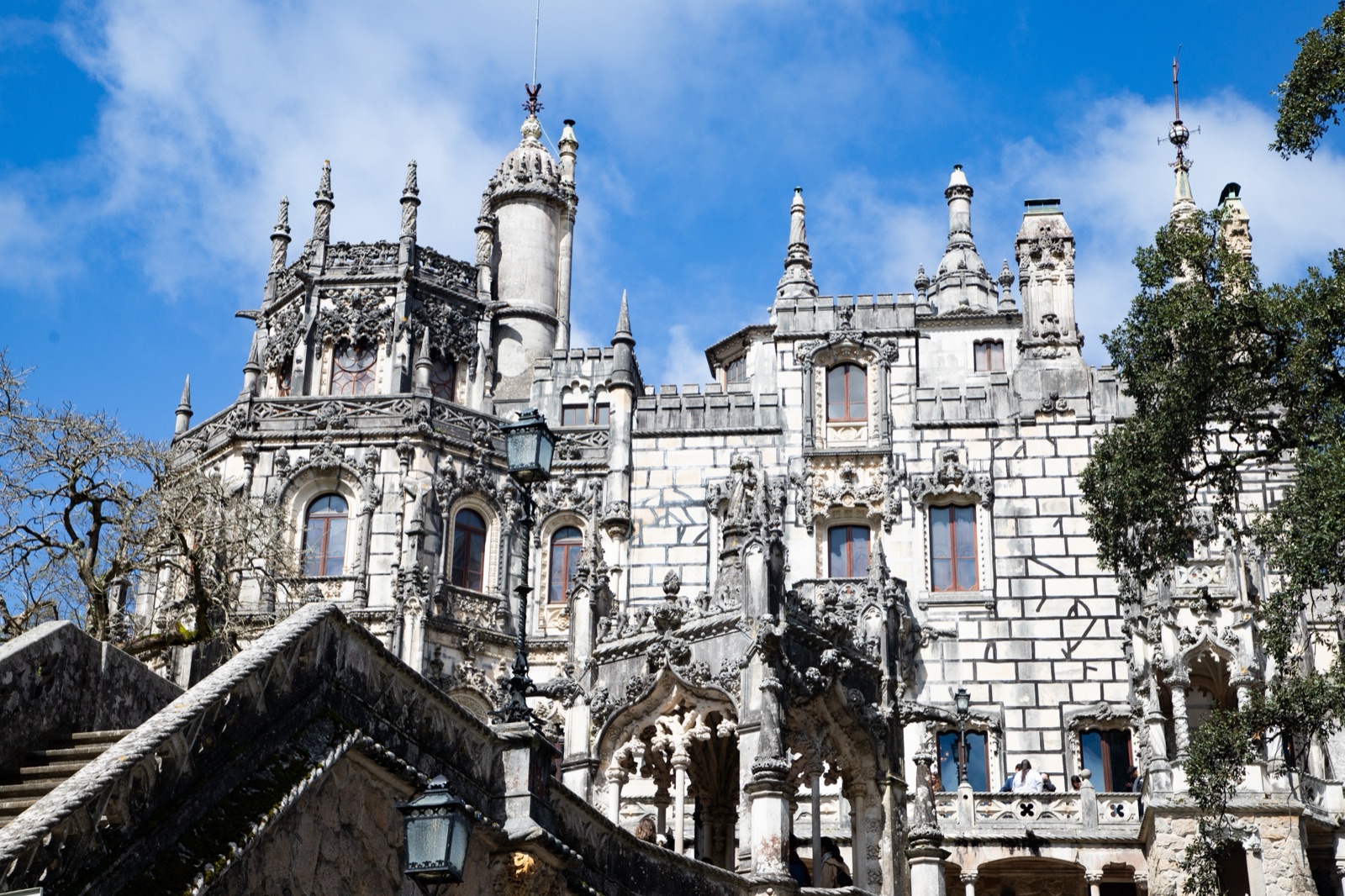 The carved grey stone towers and pinnacles of the palace at Quinta da Regaleira, seen from below a stone staircase